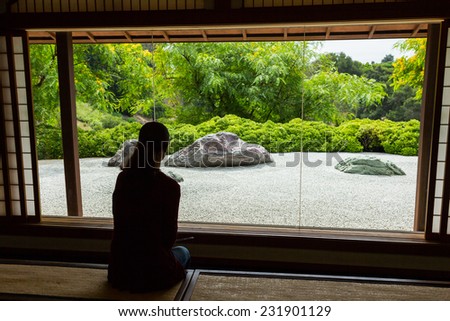 Woman looking through a window at a Japanese Zen Rock Garden.