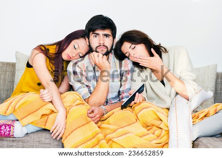 Three friends watching the tv. Two tired girls are sleeping. The man is looking with interest.