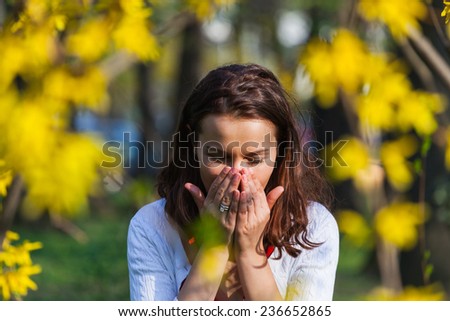Woman with a flu or an allergy is sneezing while standing outside, in a park