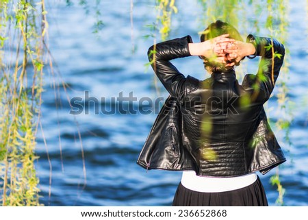 Back of a young woman with leather jacket looking at a lake