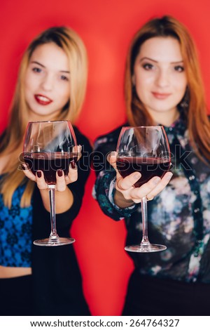 Two smiling woman holding glasses of red wine. Focus on the foreground. The women are in blur.