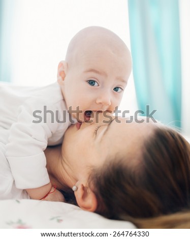 Closeup of a baby boy biting mother\'s nose and lying on her