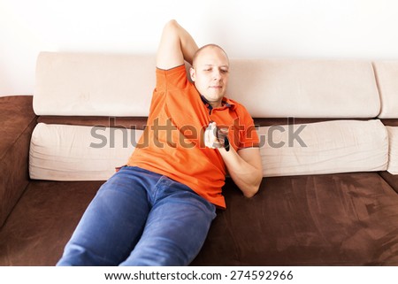 Young relaxed man lying on the couch and watching television