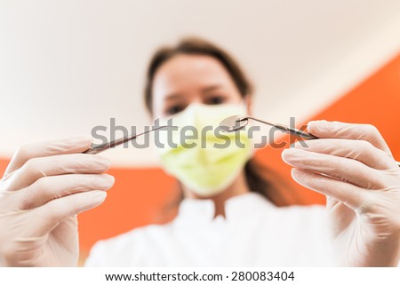 Patient\'s view of a female dentist examining with probe and mouth mirror. Image focus is on the dental instruments.
