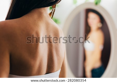 Sensual blurry pose of a back of a woman wearing bra and looking in the mirror. Focus on the woman\'s back