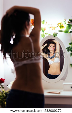 Sexy pose of an attractive woman in white bra looking in the mirror and holding hair with hands