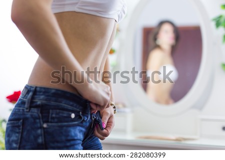 Torso of a fit woman undressing the jeans and looking in the mirror