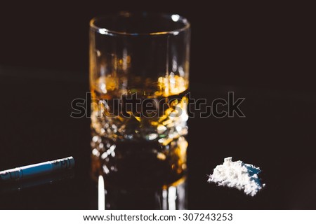 Closeup of a glass with alcohol, cigarette and drugs on black background