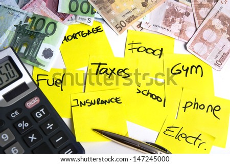Calculator and banknotes on a table filled with yellow post it notes regarding cost of living: mortgage, taxes, fuel, food, school, phone, insurance, gym and electricity