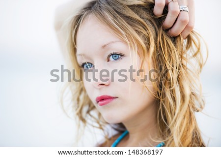 Beautiful sexy young woman with blonde hair, pale skin and wonderful blue eyes with the hand on her hair and fingers holding a lock of hair