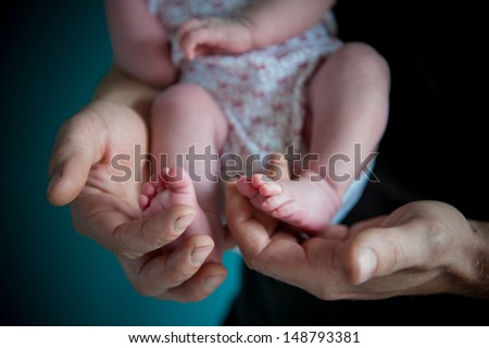Father holding sweetly with his hands the tiny feet of his newborn lovely daughter