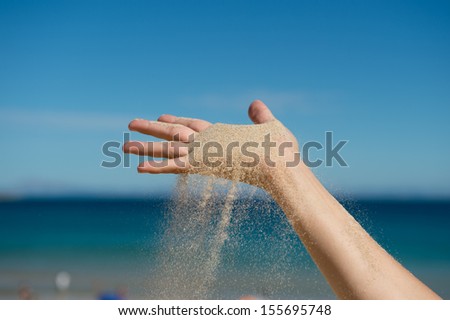 Sand grains falling for a caucasian hand at the beach blue background