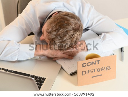 Young Student or Businessman Overwhelmed sleeping with Dont Disturb sign written on cardboard