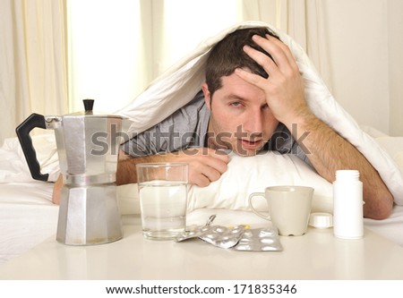 exhausted young Man in bed with coffee, water and tablets suffering hangover and headache