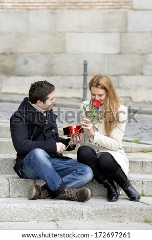 Romantic couple sitting on stairs on Valentines day with heart box and rose