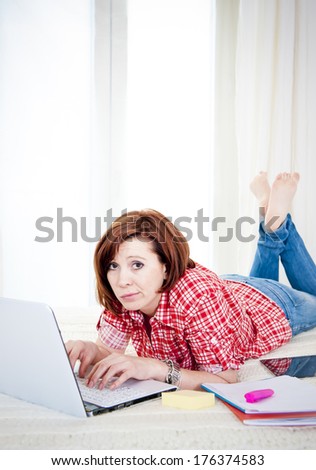 bored red hair student or business woman lying down working on her computer wearing a red shirt on white background