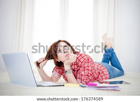 happy red haired student or business woman lying down working on her computer thinking about her future wearing a red shirt on white background