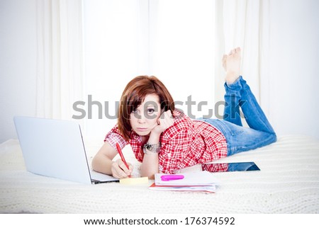 bored red hair student or business woman lying down working on her computer wearing a red shirt on white background