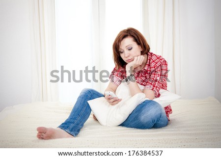 red haired student or business woman sad and worried sending or receiving a message on her mobile cell phone on a white background