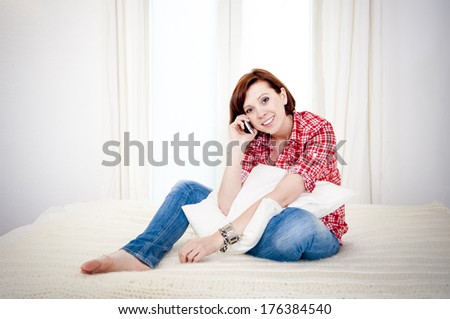 red haired business woman or student on couch or bed happy on her mobile cell phone wearing a red shirt on a white background