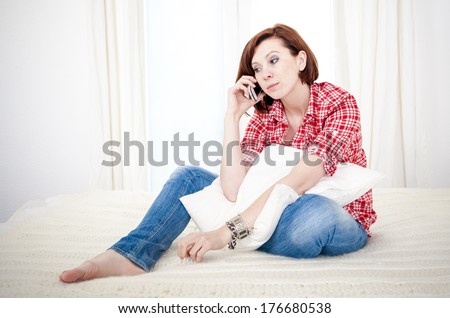 red haired student or business woman sad and worried talking on her mobile cell phone wearing a red shirt on a white background