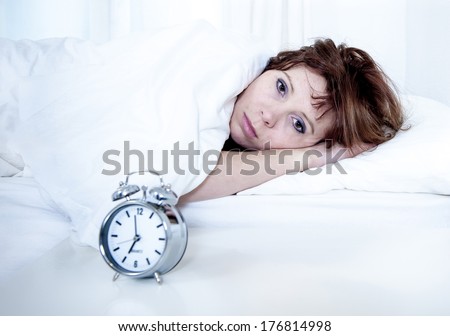 woman with red hair in her bed with insomnia and nightmare can't sleep waiting for her alarm clock to go off on a white background