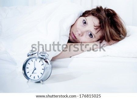 woman with red hair in her bed with insomnia and nightmare can\'t sleep waiting for her alarm clock to go off on a white background