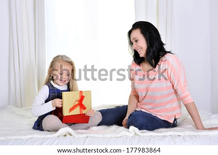 happy young mother holding remote and playful daughter watching television tv lying on bed together