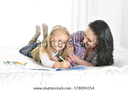 happy blonde hair daughter with her brunette mother sitting on bed working together on computer
