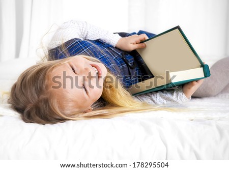 happy cute blonde haired school girl wearing a school uniform reading a book sitting on the bed