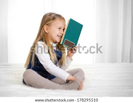 happy cute blonde haired school girl wearing a school uniform reading a book sitting on the bed