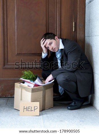 desperate business man in stress fired from job sitting on edgy street corner with office belongings in cardboard box and asking for help