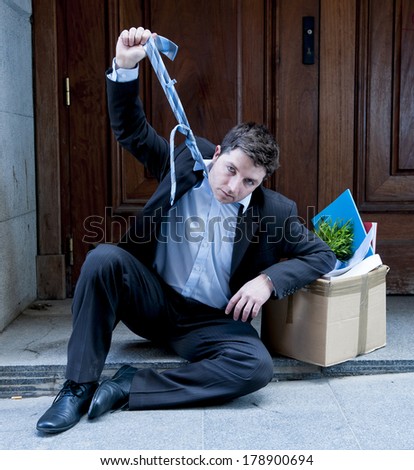 desperate business man in stress fired from job sitting on edgy street corner with office belongings in cardboard box
