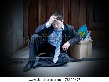 desperate business man in stress fired from job sitting on edgy street corner with office belongings in cardboard box