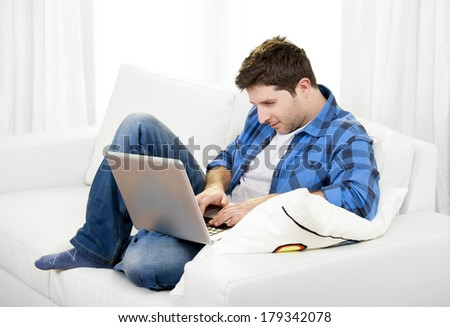 Young attractive relaxed man in casual clothes working with Computer  sitting on couch at home