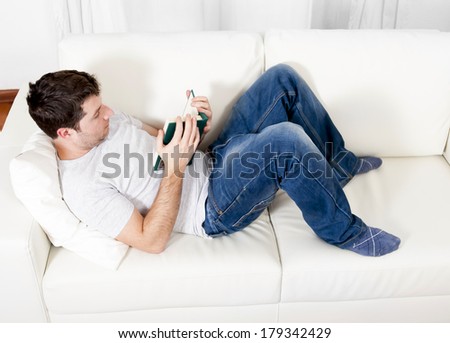 young attractive man reading book lying relaxed on couch or studying