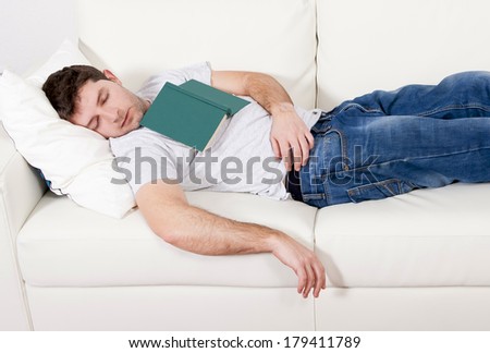 tired young man sleeping on couch with book on lap after reading