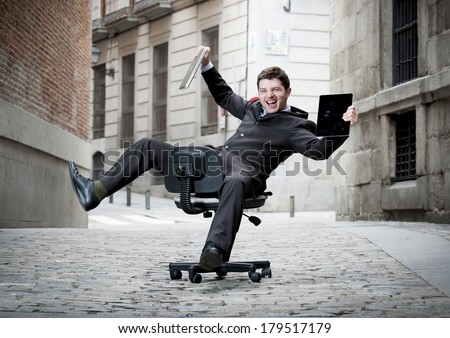 Happy crazy business man rolling downhill on chair with computer and tablet