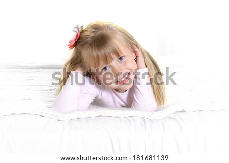 Cute little blonde girl with sweet face expression smiling and lying happy on bed at home in children lifestyle concept