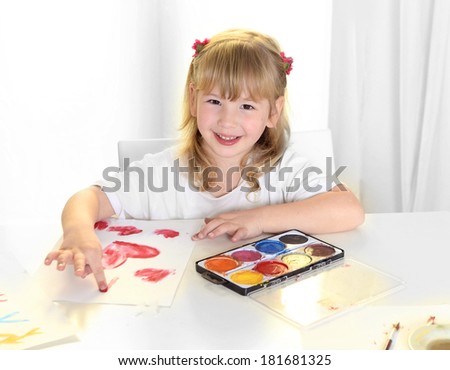 Cute beautiful little blonde girl with sweet face expression having fun and painting red hearts with fingers in watercolors