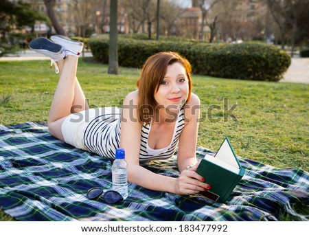 pretty red haired woman reading a book or novel in a park