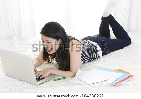 young beautiful asian chinese student or business woman at home lying on bed in casual clothes studying and working with computer and notepads before exam