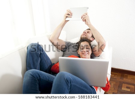 young happy couple lying on a sofa or couch working on their laptop and tablet together relaxed and cozy in a white living room
