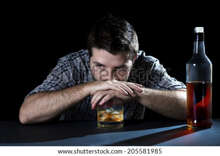 grunge young alcoholic man drunk at the table of a bar looking wasted and depressed with hands on whiskey glass isolated black background representing alcohol abuse, addiction and alcoholism concept