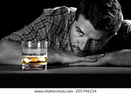 alcoholic drunk and wasted but attractive man sitting at table looking whiskey glass thinking in his alcohol addiction problem trying to avoid temptation and desire to drink in alcoholism concept
