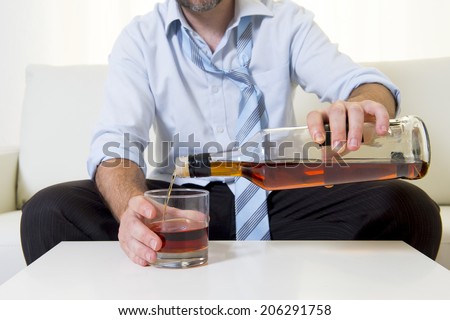 caucasian businessman alcoholic wearing a blue work shirt and tie drunk and drinking  Scotch or Whisky sitting on a sofa at home after a long day or week of work on a white background.