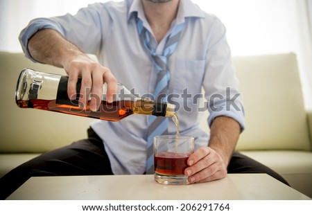 caucasian businessman alcoholic wearing a blue work shirt and tie drunk and drinking  Scotch or Whisky or Whiskey sitting on a sofa at home after a long day or week of work on a white background.