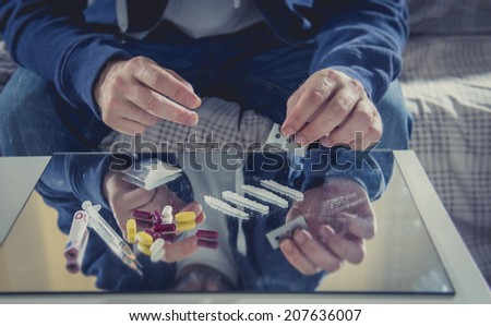 young drug addict man on hood sniffing cocaine on mirror with rolled banknote at home alone representing the concept of young people using and abusing drugs