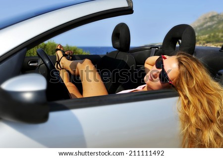 young sexy chic woman with sunglasses lying on cabrio sport car on the beach in relaxed summer holidays having a sunbath in front of the sea