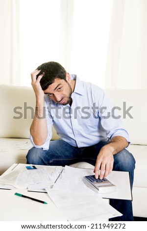 young attractive latin american business man at home sitting on sofa with credit card and calculator accounting costs, charges, taxes and mortgage for paying bills looking worried and stressed